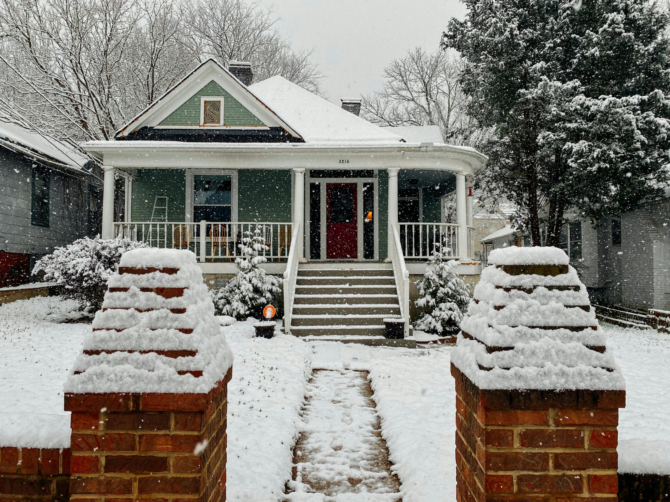 A picturesque bungalow with a snow-covered roof and trees depicting a serene winter scene.